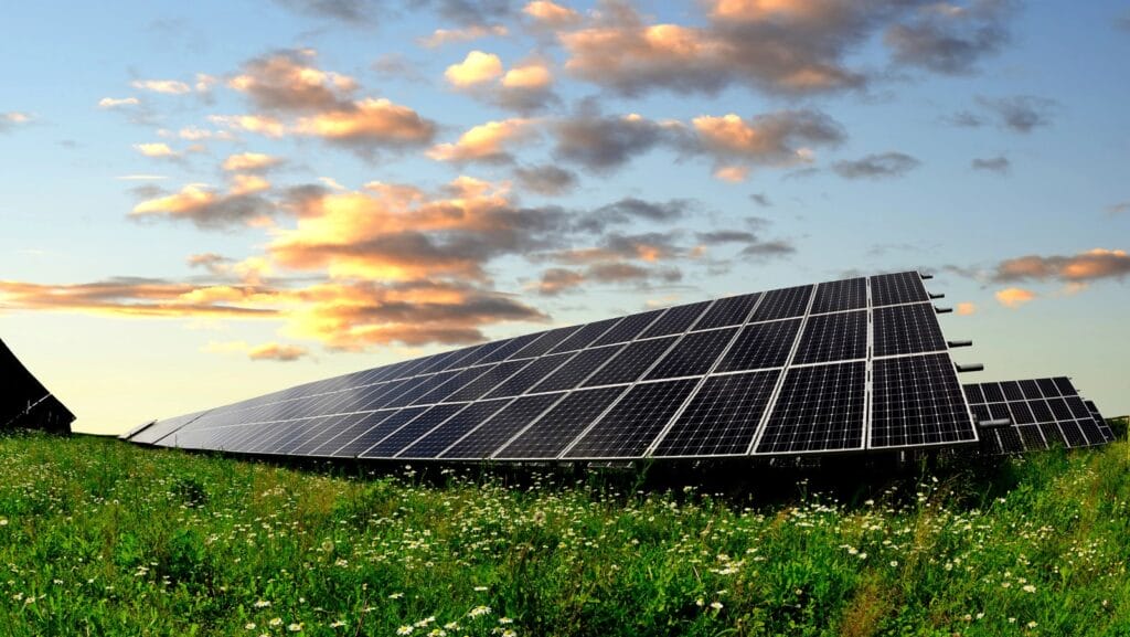 Efficient solar energy panels set amidst lush green grass, under a beautiful sky with few clouds and a warm, orange hue, showcasing the harmony of renewable energy with nature