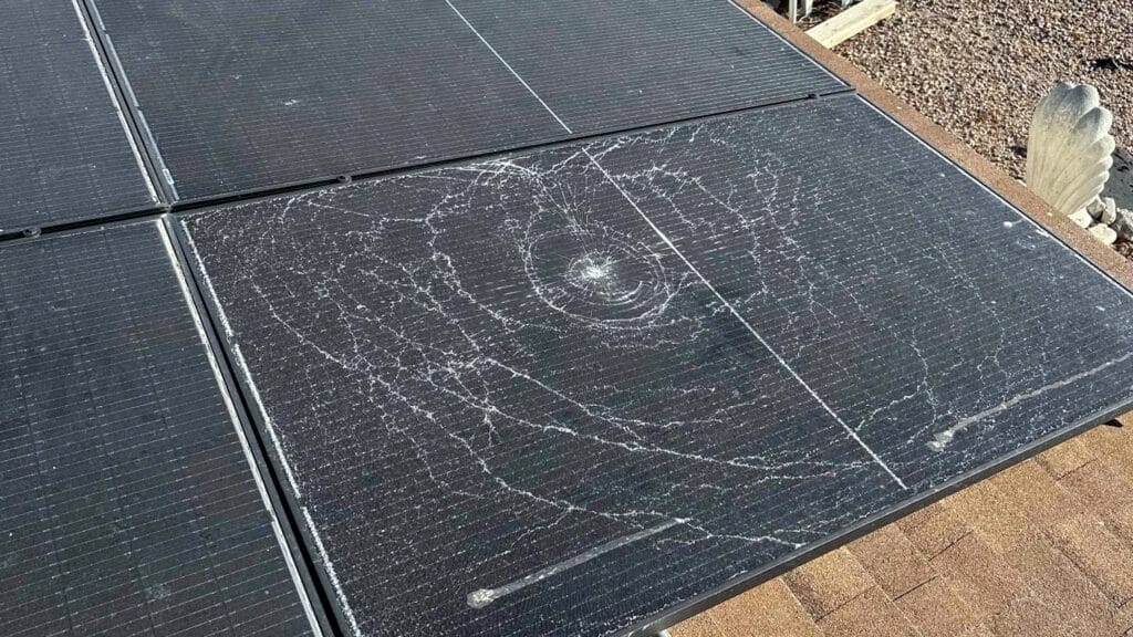 Close-up of a cracked solar panel with visible circular damage and multiple fracture lines.
