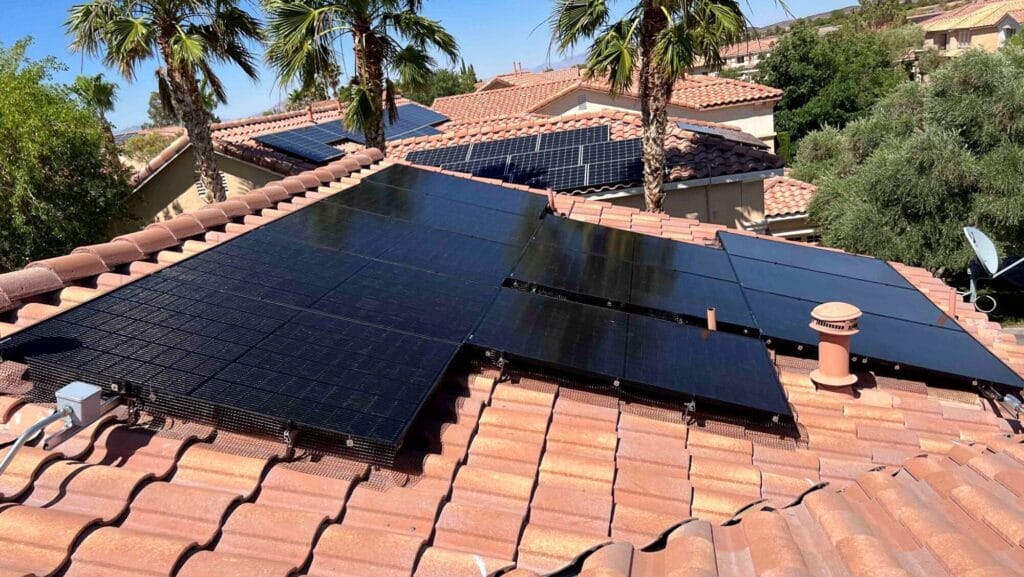 Residential rooftop with installed rigid solar panels surrounded by trees and a clear sky.