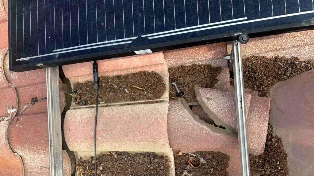 Close-up of dust and debris accumulated in roof tile channels beneath removed solar panels.
