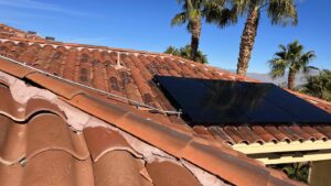 A cluster of black solar panels sits nestled among red tile roofing and palm trees, part of a home system built for charging an EV with solar panels in Las Vegas.